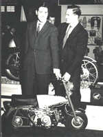 Geoff 
            Duke (L) and Jonathan Glover at the Honda booth, at the Earls Court show, London in 1962.  The first time Honda had displayed their complete model range at E.C.